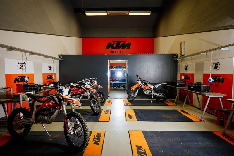 Boxengasse der eDirtarena mit KTM Freeride E Elektro-Motorr&auml;dern und nummerierten Fahrerpl&auml;tzen