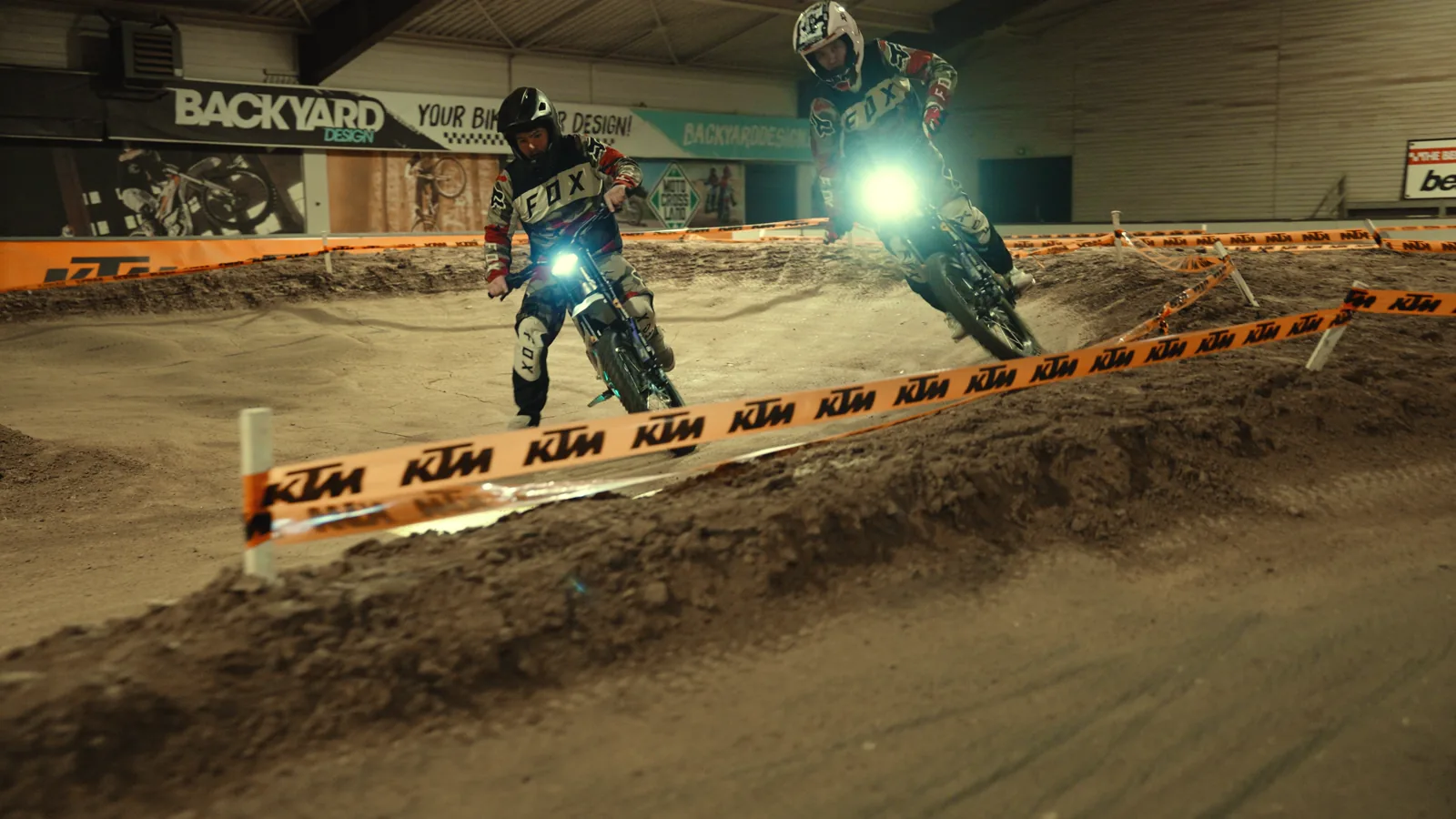 Zwei Erwachsene fahren mit Elektro-Motocross-Motorrädern über die Indoor-Strecke
