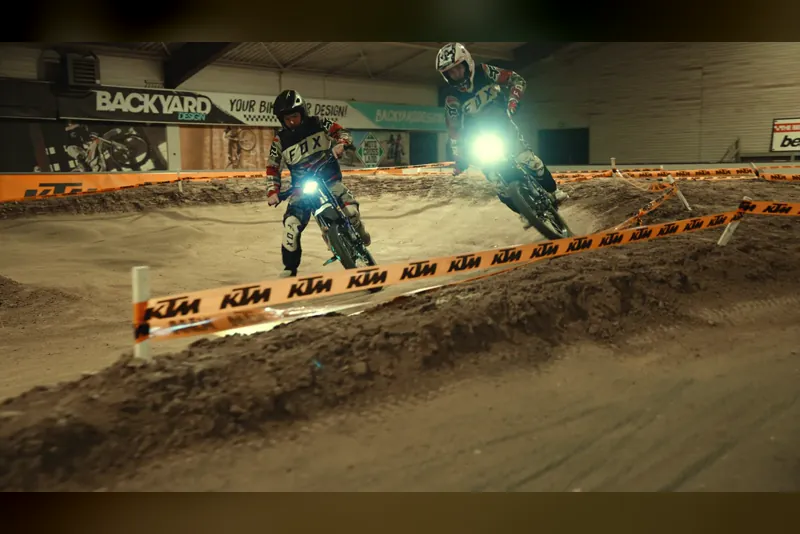 Zwei Erwachsene fahren mit Elektro-Motocross-Motorrädern über die Indoor-Strecke