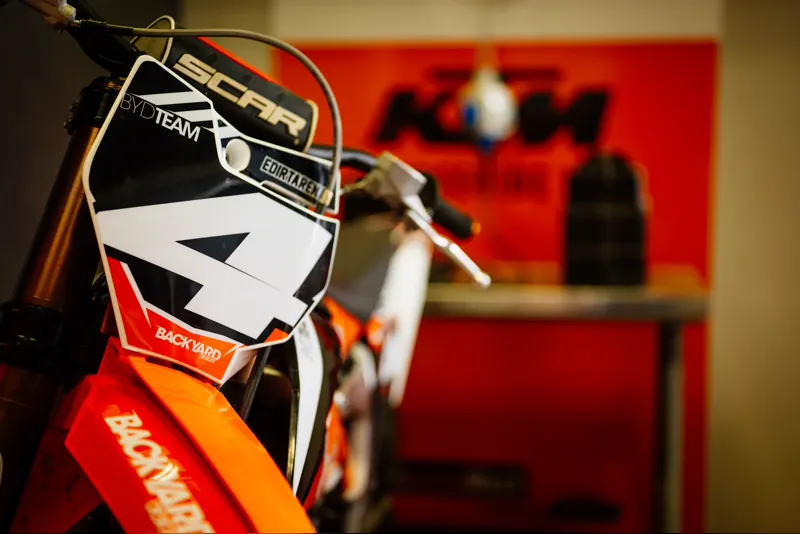 Motocross-Motorrad mit Startnummer 4 vor der orangen KTM-Wand