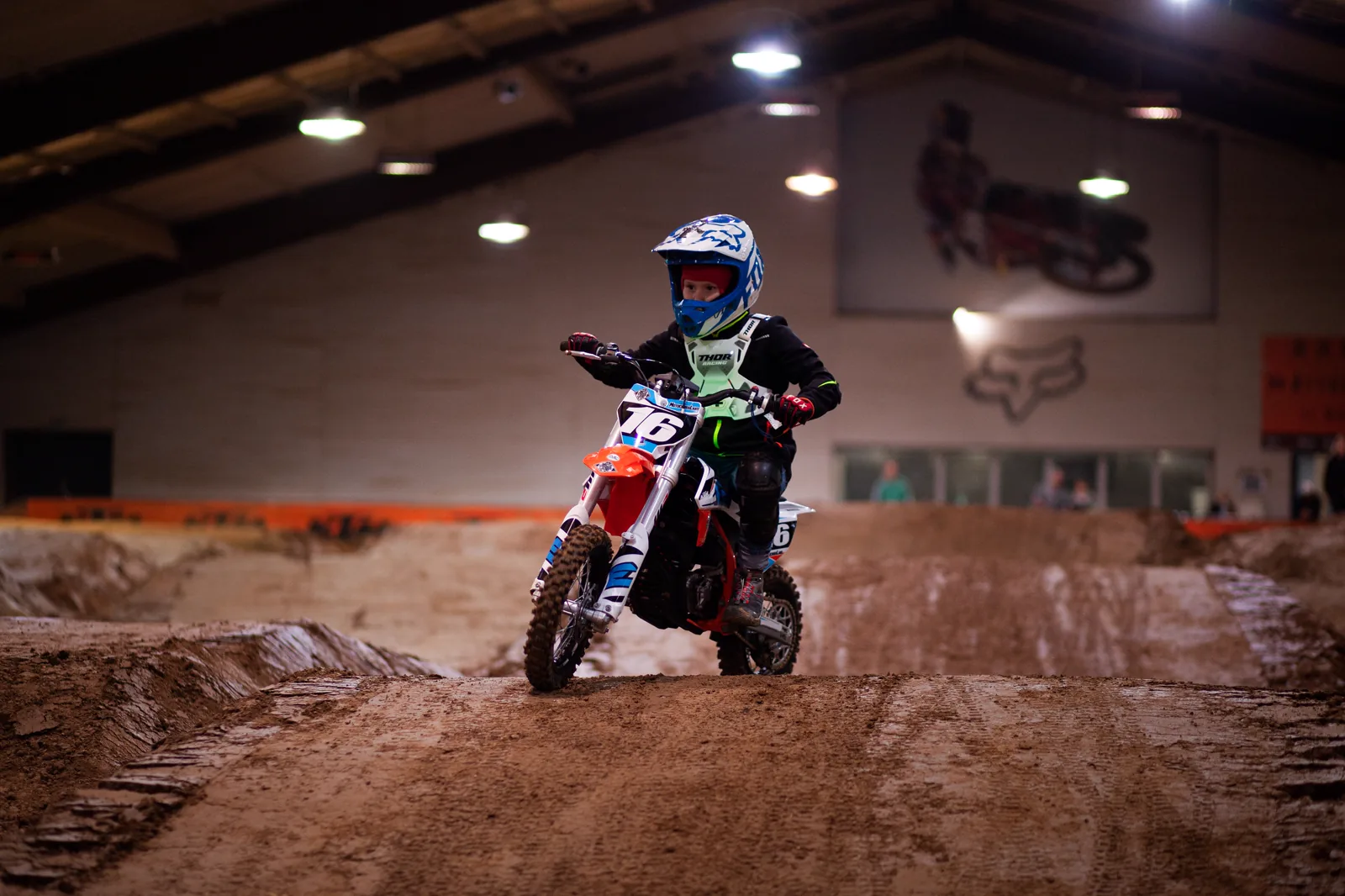 Kind auf einem grünen Elektro-Motorrad auf der Indoor-Motocross-Strecke
