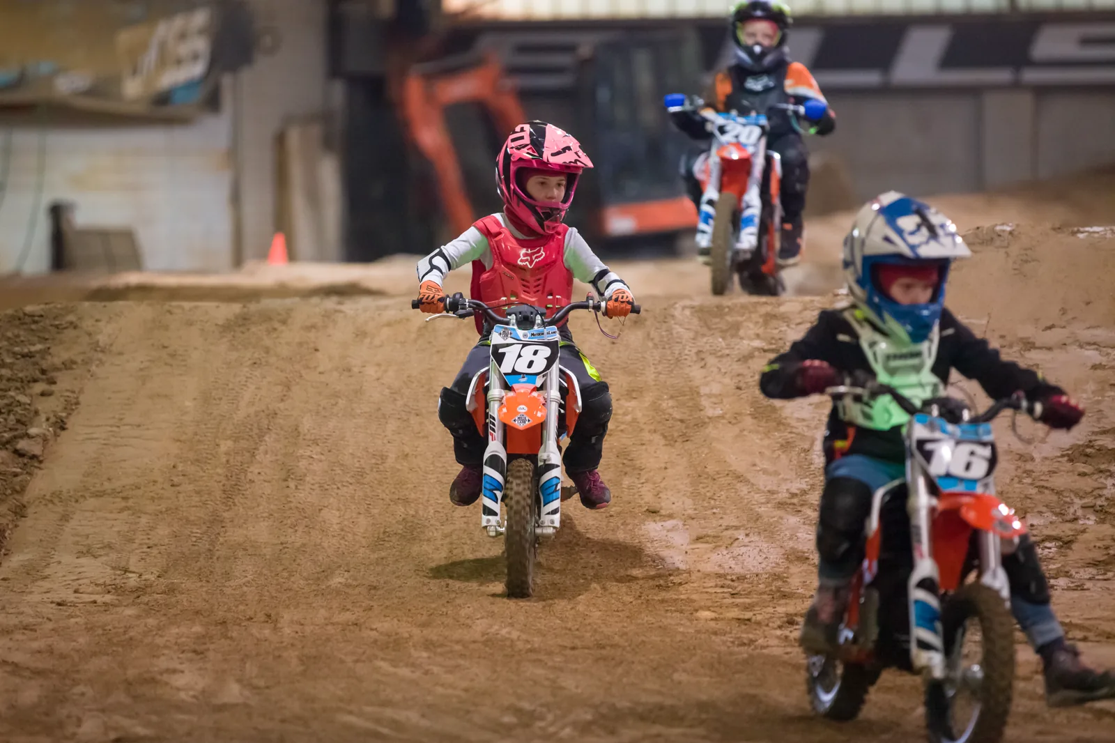 Drei Kinder fahren im Einsteigerkurs gemeinsam über die Indoor-Motocross-Strecke