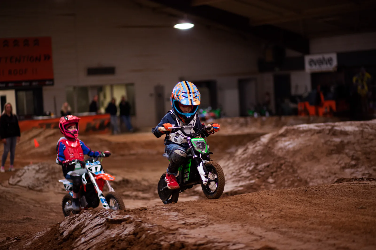 Nebeneinander über die Wellen Zwei Kinder fahren nebeneinander über die Wellen der Indoor-Motocross-Strecke