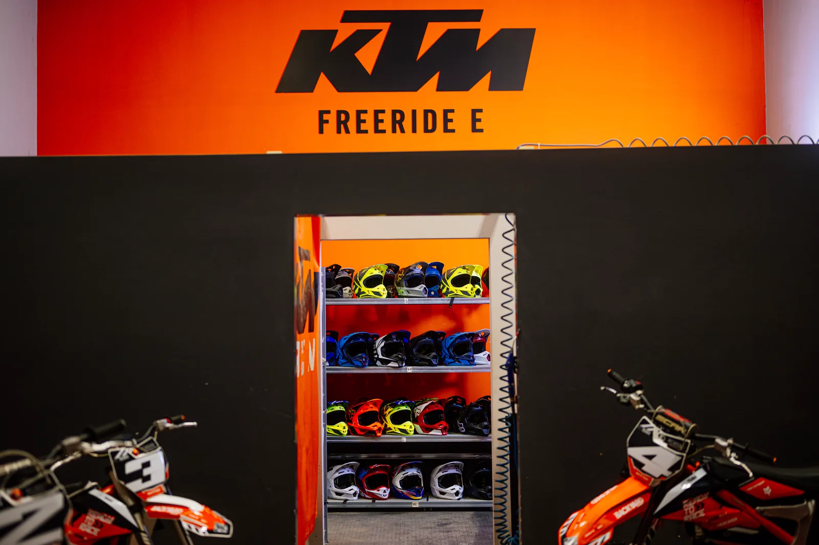 Werkstattbereich mit KTM-Freeride-E-Schriftzug und Regal voller Leihhelme